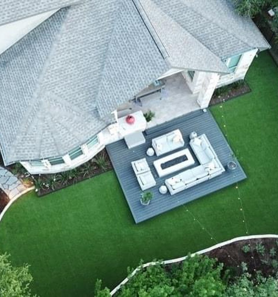 Bee Cave backyard with a composite deck, turf island, and flagstone patio under live oaks