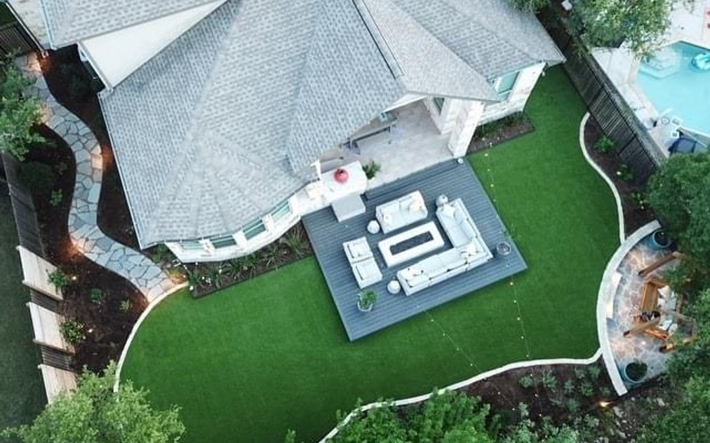 Aerial view of a backyard deck with a flagstone patio and turf under mature live oaks in Bee Cave, near Austin