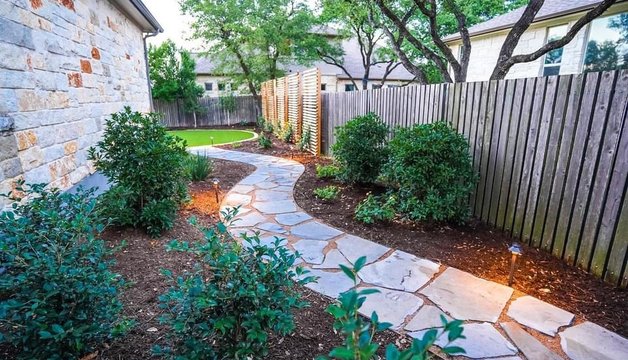 Bee Cave backyard design with a flagstone pathway, planting beds, privacy screen, and turf