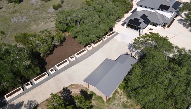 Aerial overview of a Driftwood estate landscape design with raised limestone beds and a paver driveway