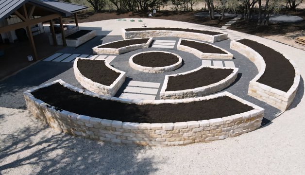 Driftwood estate landscape with raised limestone beds, stone pavers, and a formal walkway
