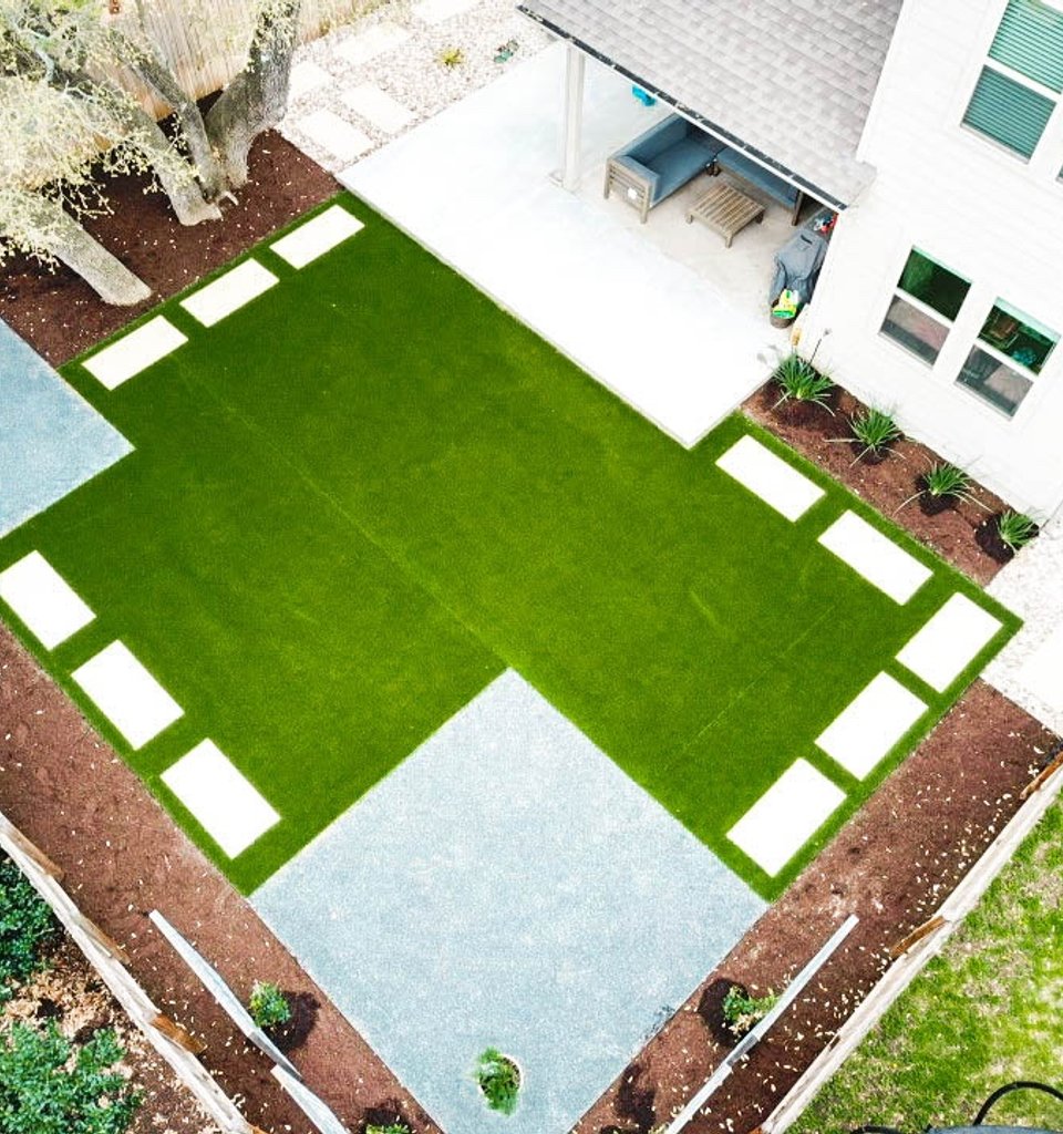 Round Rock backyard with cream pavers set into synthetic turf in a checkerboard pattern