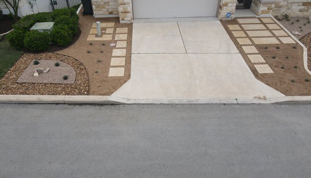 Front yard landscape design in Spicewood with a paver driveway, gravel, and ornamental grasses