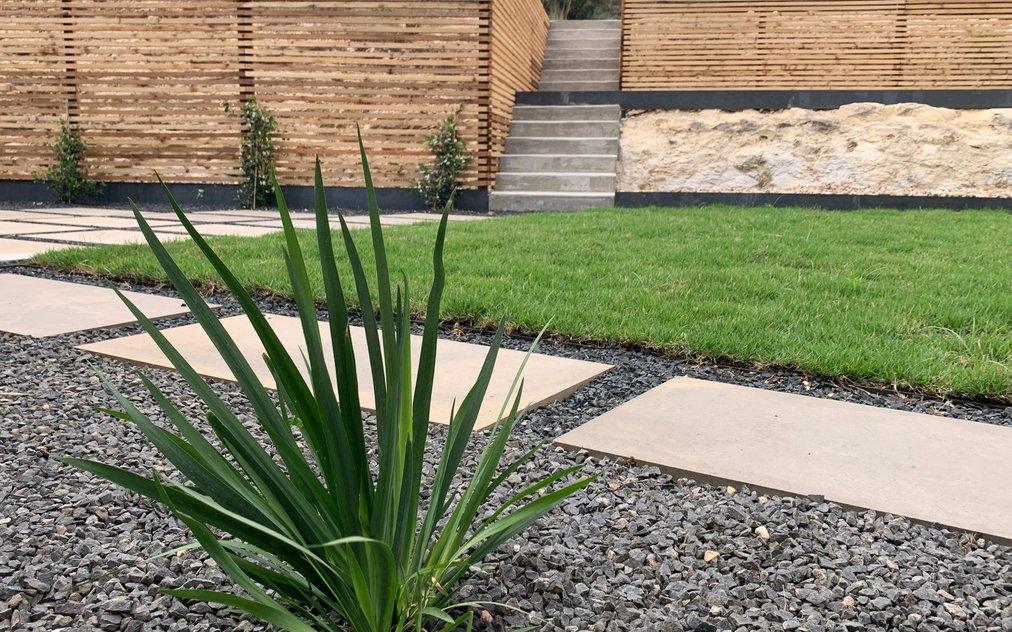 Terraced Westlake Hills backyard with stepping stones, gravel, sod, concrete steps, and a horizontal slat fence