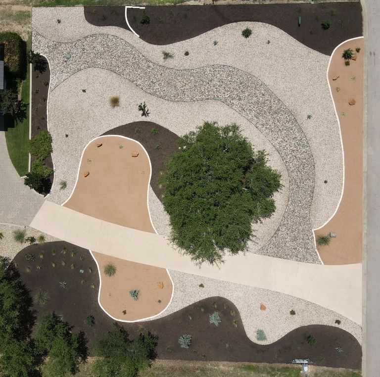 Aerial xeriscape design with crushed granite, river rock, and mulch zones around a live oak in Dripping Springs